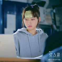 a young woman with a sticky note on her head sitting in front of a laptop computer