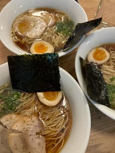 two bowls of ramen with chopsticks and an egg in the middle on a wooden table