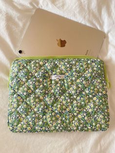 an apple laptop computer sitting on top of a flowery bag next to a white bed