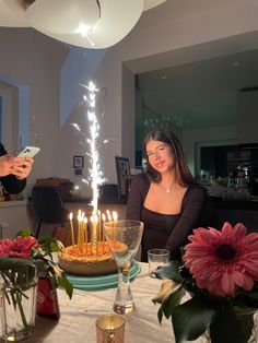 a woman sitting at a table in front of a cake with lit candles on it