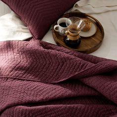 a tray with two coffee cups on it next to a red quilted comforter