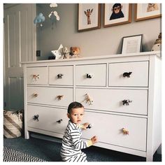 a little boy standing in front of a white dresser with toy animals on it's drawers