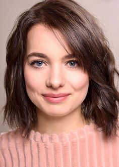 a close up of a person wearing a pink sweater and smiling at the camera with blue eyes