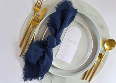 a place setting with napkins, gold forks and silverware on a marble plate