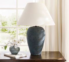 a blue vase sitting on top of a wooden table next to a white lampshade