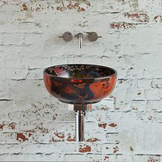 a bathroom sink sitting on top of a metal faucet next to a white brick wall