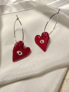 two red heart shaped earrings with eyeballs on them sitting next to a white cloth