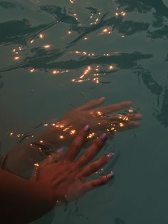 a person's hand reaching for something in the water with lights on their fingers