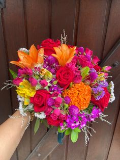 a bouquet of colorful flowers is being held by a person's hand in front of a wooden door