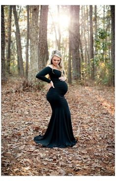 a pregnant woman standing in the woods wearing a long black dress with her hands on her hips