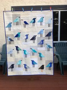 a blue and white quilt with birds on it sitting in front of two green chairs