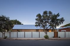 a house that is next to a tree in the middle of the street with a fence around it