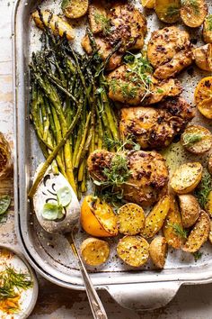 a pan filled with chicken, potatoes and asparagus on top of a table