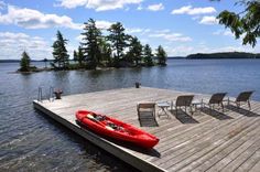 a red kayak sitting on top of a wooden dock next to chairs and trees