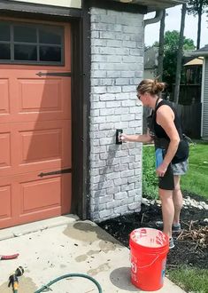 a woman is painting the side of a brick building with a sprayer on it