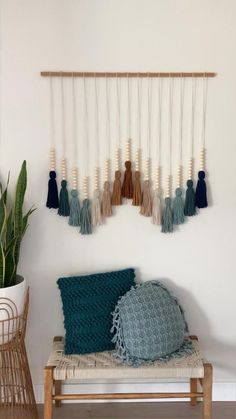 a wall hanging with several tassels on it and a chair in front of it