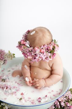 a baby sitting in a bowl surrounded by flowers