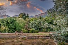 a bench sitting in the middle of a field with mountains in the background at sunset