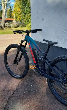 a blue and red mountain bike parked next to a building with trees in the background