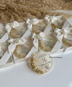 wedding favors in white boxes with gold glitters and bows on them, sitting on a table