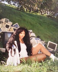 a woman sitting in the grass next to a pile of computer equipment