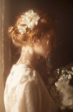 a woman with red hair and flowers in her hair is looking at something outside the window