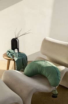 two white chairs with green pillows and a black vase on the table in front of them