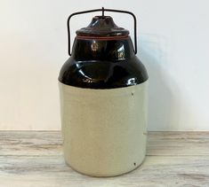 a black and white ceramic jar sitting on top of a wooden table next to a wall