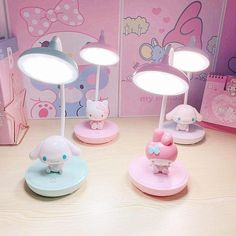 three hello kitty desk lamps sitting on top of a wooden table next to a pink wall