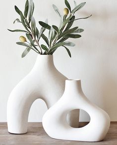 two white vases sitting on top of a wooden table next to each other with plants in them