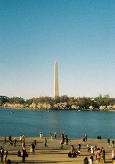 many people are standing near the water and in front of a tall obelisk