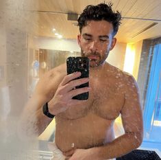 a shirtless man taking a selfie in the shower