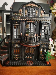 a black doll house with lots of windows and decorations on the front door, next to a stair case