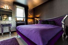 a bedroom with purple bedding and chandelier in the corner, along with black walls