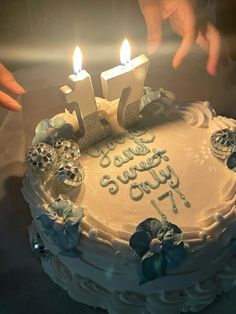 a birthday cake with two candles on it and someone reaching out to touch the frosting