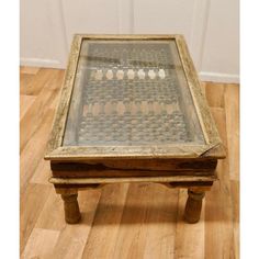 an old wooden table with glass top on wood floor next to white wall and door