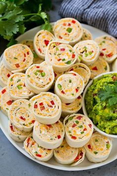 a plate full of taco pinwheels with guacamole on the side