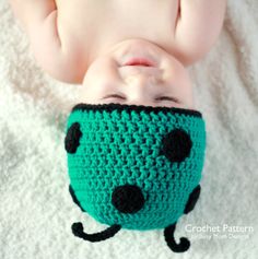 the baby is wearing a green crocheted hat with black spots on it's face