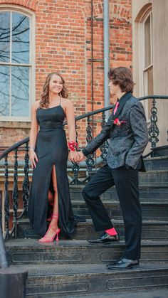 a woman in a black dress and man in a suit standing on steps holding hands