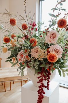 a white vase filled with lots of flowers on top of a table next to a window