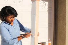 a woman is painting the side of a house with paint rollers and a brush