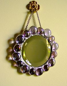 a mirror hanging from a chain on the wall with beads and chains attached to it