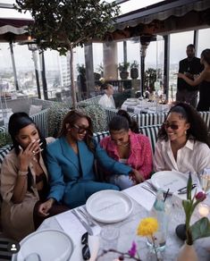 three women sitting at a table with plates and drinks in front of them, talking on the phone