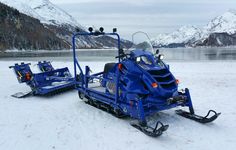 two snowmobiles are parked in the snow near some water and mountains with snow on them