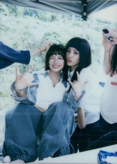 two young women sitting next to each other with their hands in the air and one pointing