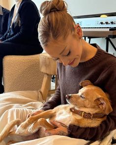 a woman sitting on a bed holding a brown and white dog in her lap while another person sits behind her