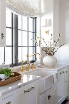 a white kitchen with gold faucets and marble counter tops is pictured in this image