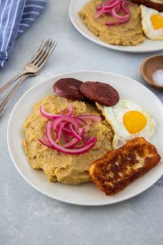 two white plates topped with breakfast foods on top of a gray tablecloth next to silverware