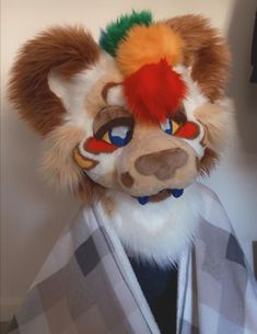 a stuffed animal is wearing a robe and headdress with red, green, orange, and yellow hair