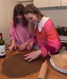 two girls are making cookies on the counter top with wine bottles and paper towels behind them